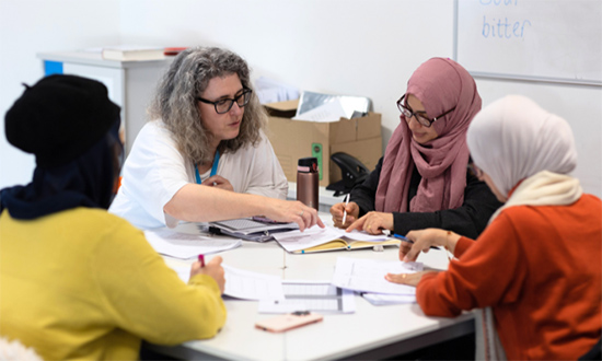 Pedair menyw yn eistedd o amgylch bwrdd yn gweithio