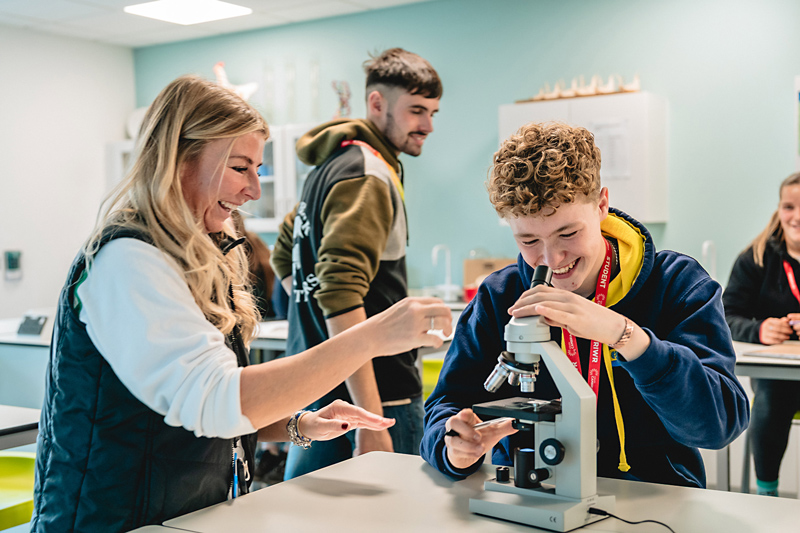 A student using a microscope with an adult